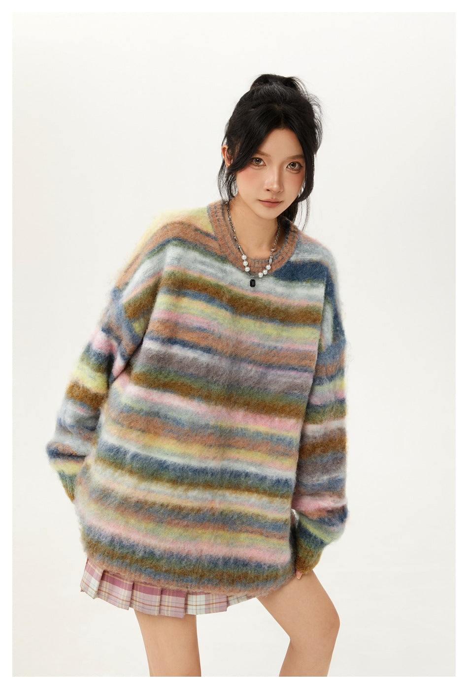 Model wearing an oversized fuzzy sweater with multicolored horizontal stripes and a pink plaid skirt.