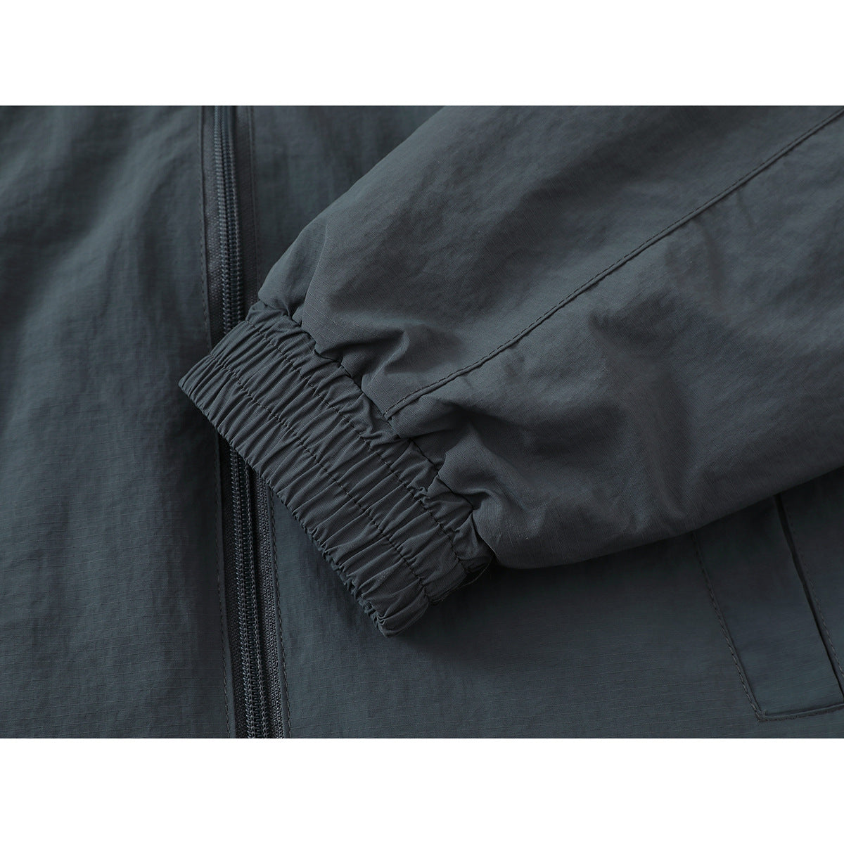 Close-up of a dark gray jacket sleeve with an elastic cuff beside the front zipper.