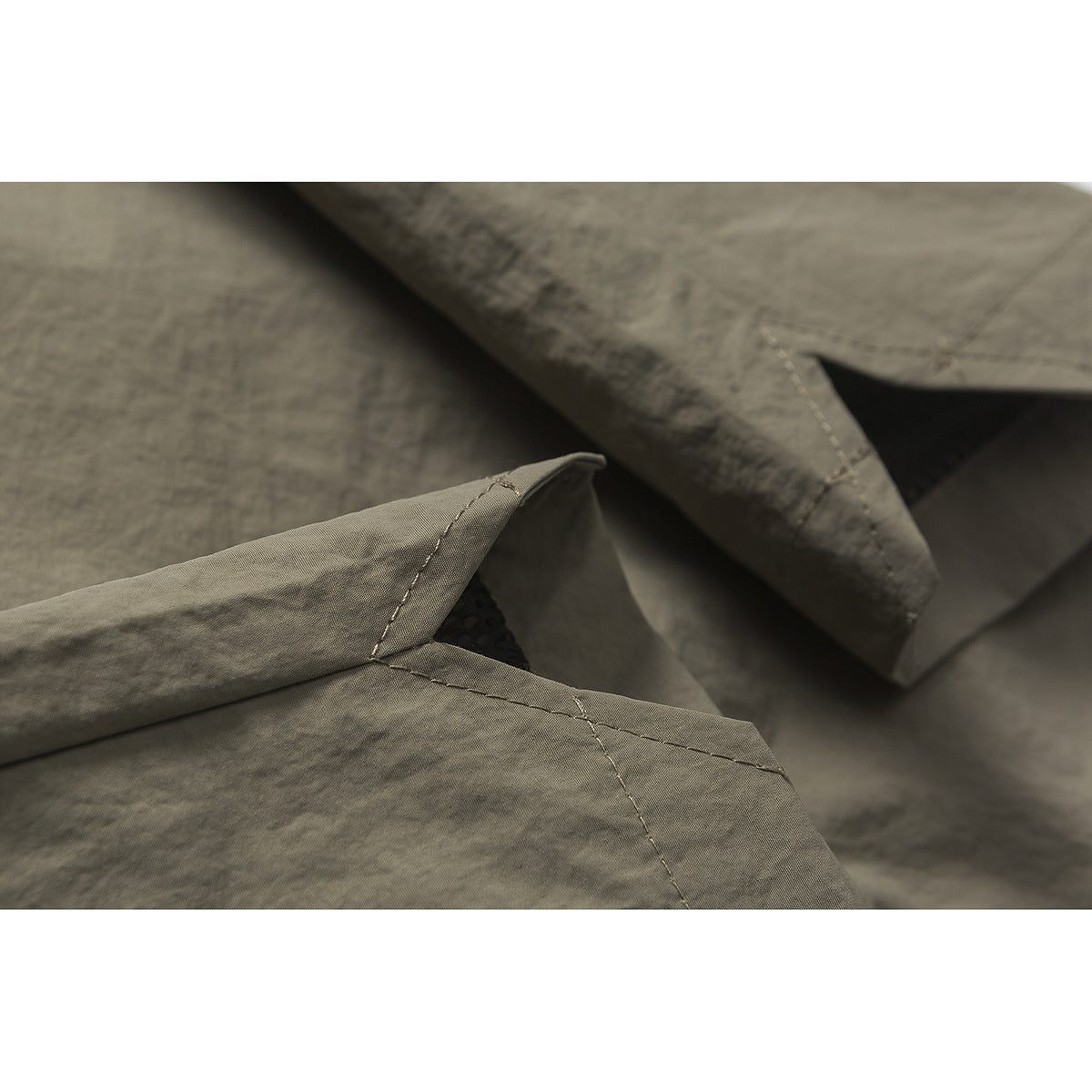 Close-up of overlapping olive-gray fabric panels and stitched seams on the shorts.