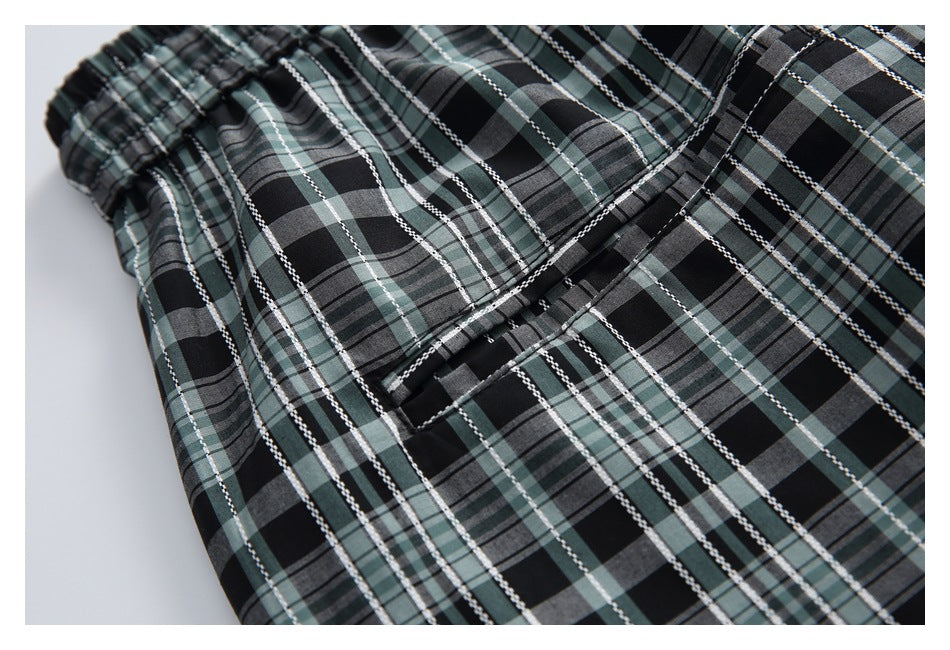Close-up of a welt pocket and stitching on black, gray, and muted green plaid trousers.