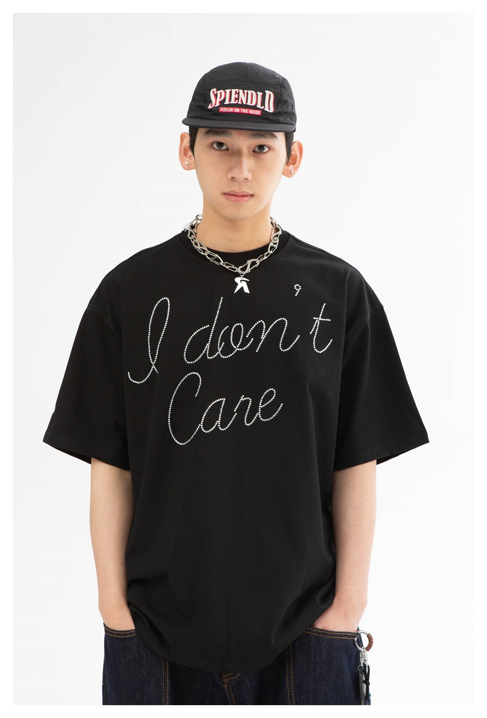 Front view of a model wearing a black oversized rhinestone-script T-shirt, black cap, and silver chain necklace.