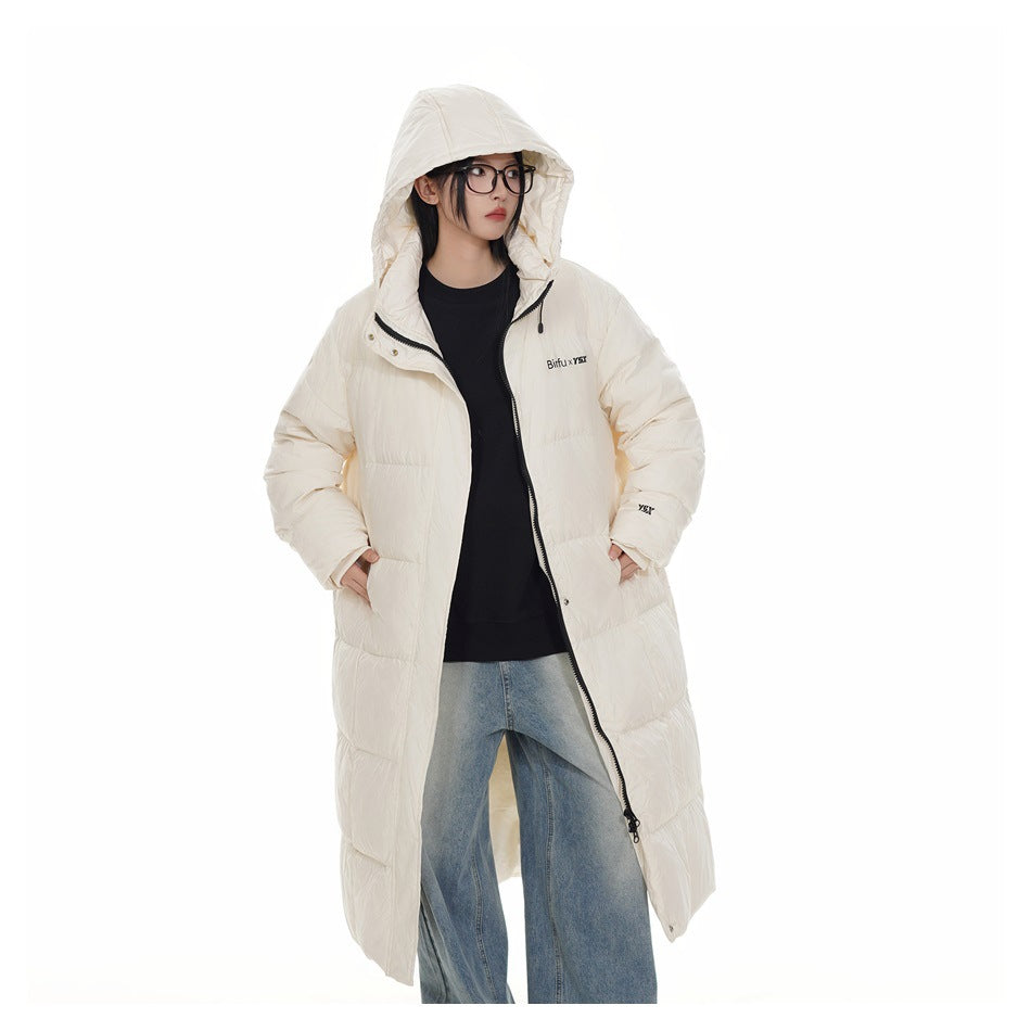 Model wearing a cream long puffer coat unzipped over a black top and jeans, hood up, hands in pockets