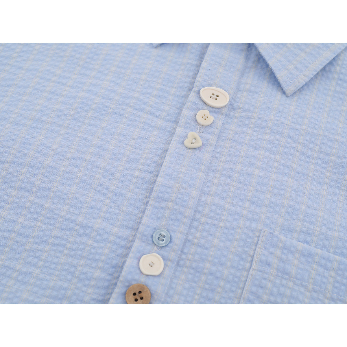 Close-up of a light blue shirt front with a subtle plaid texture, mixed buttons, and part of a chest pocket.