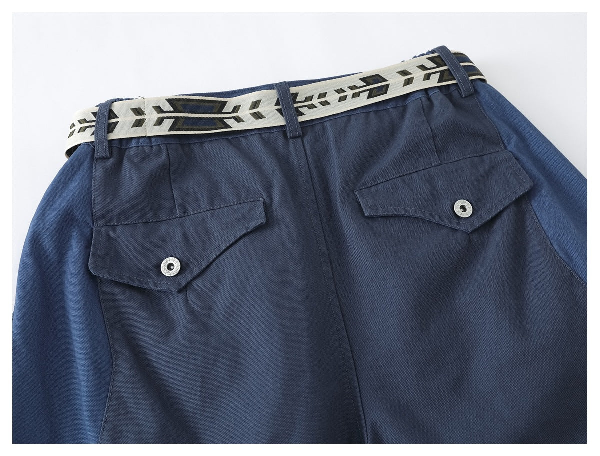 Close-up of navy trousers' back waist with two flap pockets, silver snap buttons, and a cream geometric belt.