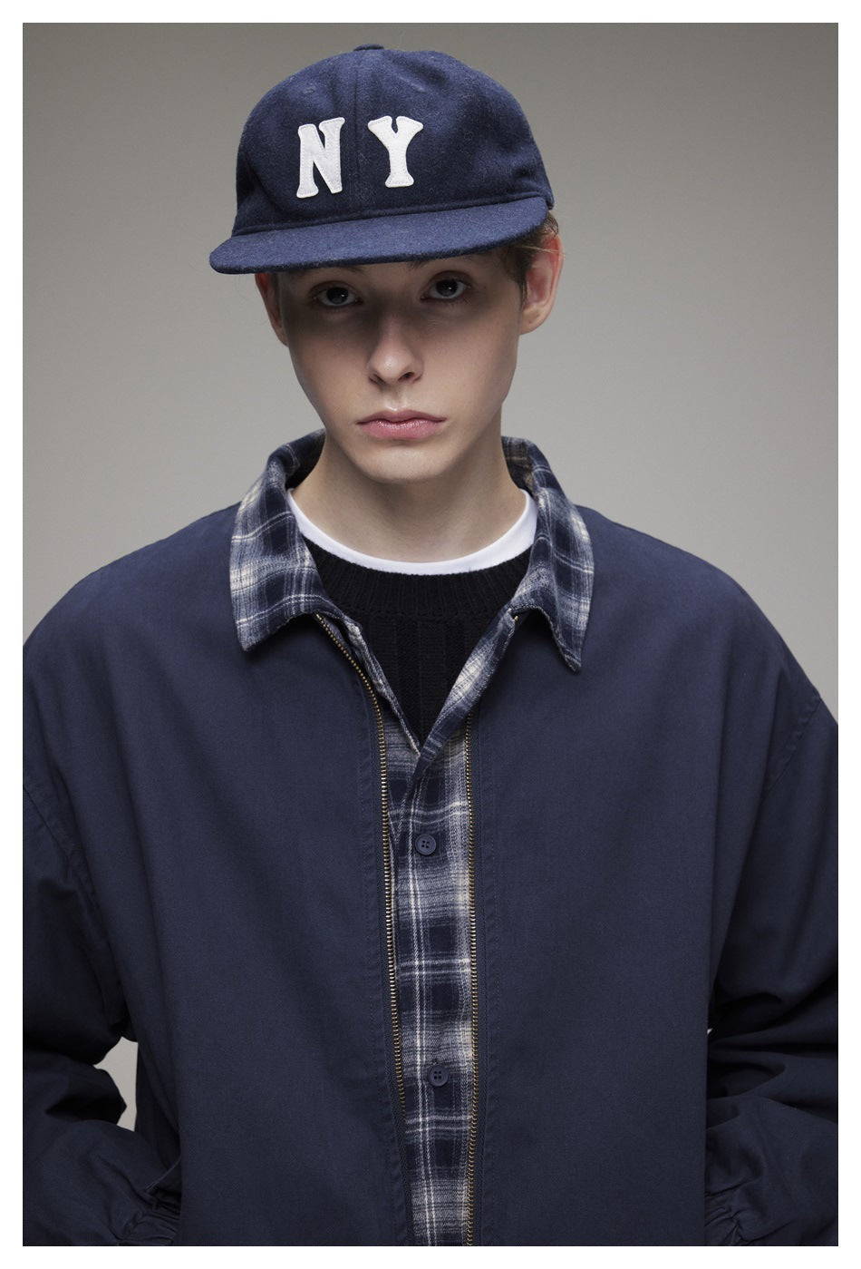 Front view of a model wearing a navy zip jacket over a gray plaid shirt.