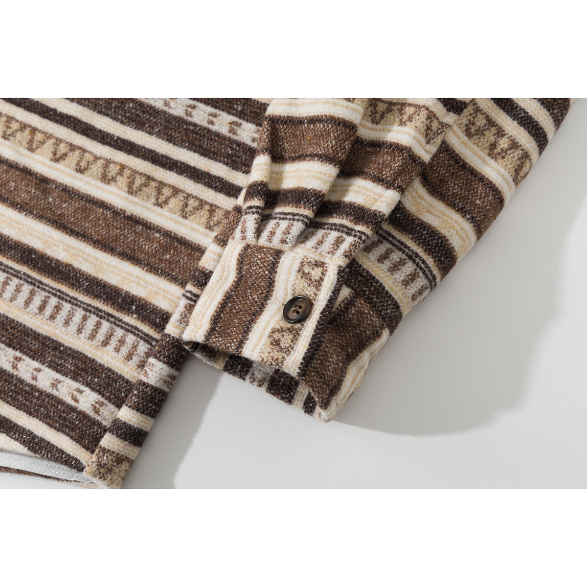 Close-up of the buttoned cuff and hem of a brown, cream, and tan patterned shirt.