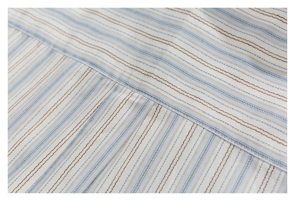 Close-up of a stitched seam joining cream fabric with fine blue and brown stripes.