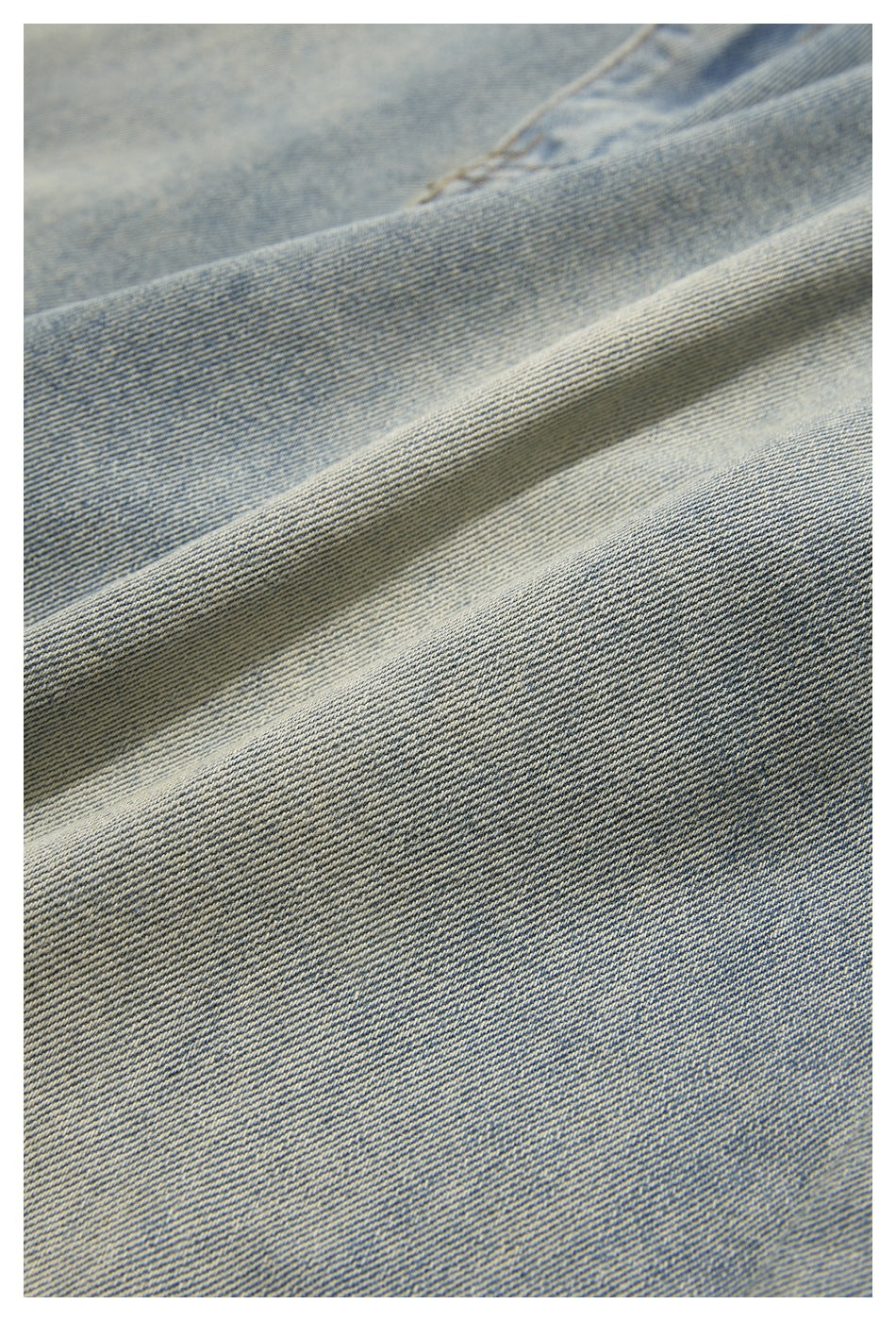 Extreme close-up of light-wash blue denim showing its diagonal twill texture and folded fabric.