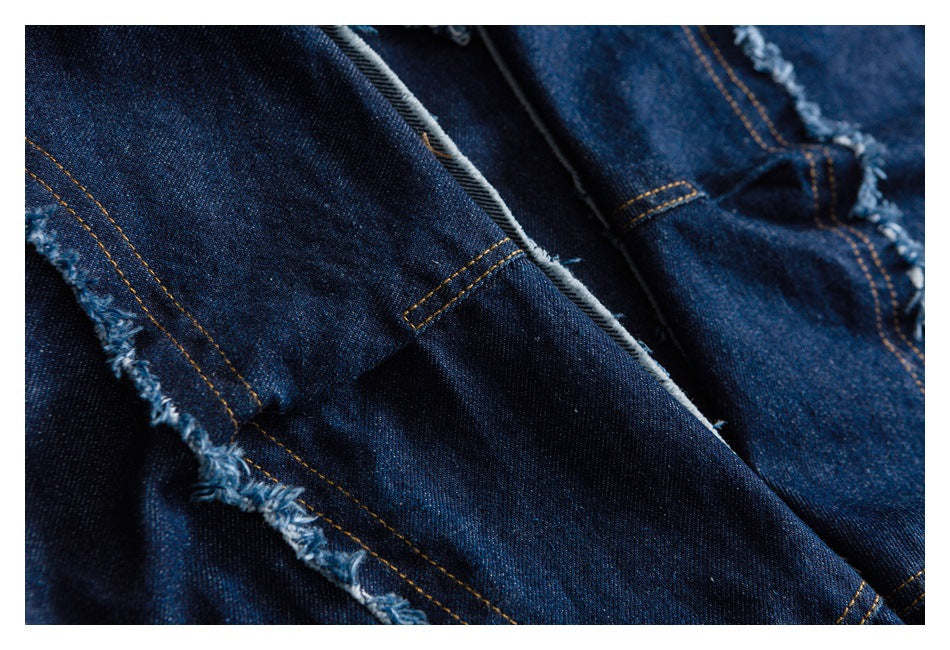 Close-up of dark indigo denim construction with gold stitching, seams, and a frayed edge.