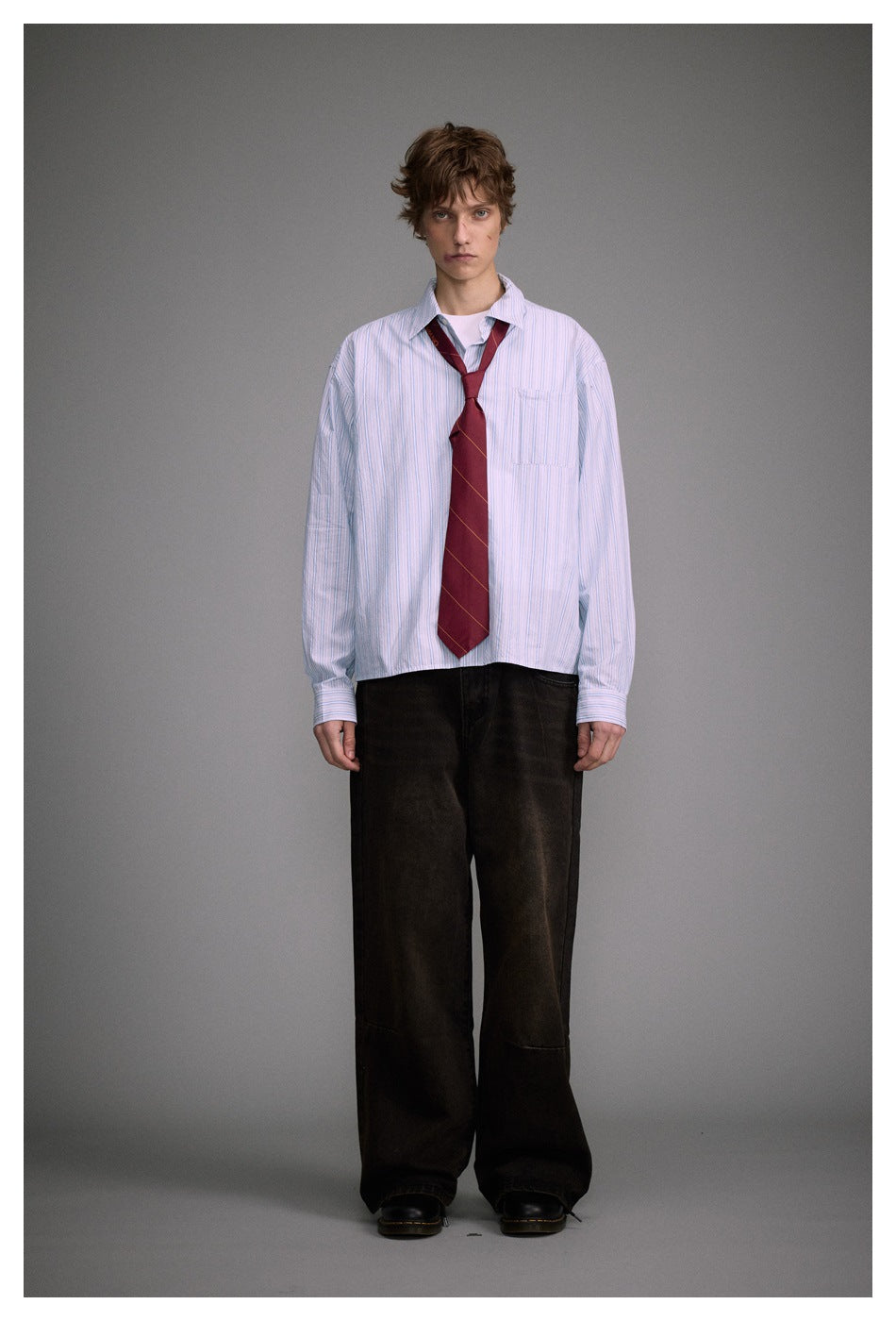 Full-length front view of a model in a pale blue striped shirt, burgundy tie, and wide black trousers.