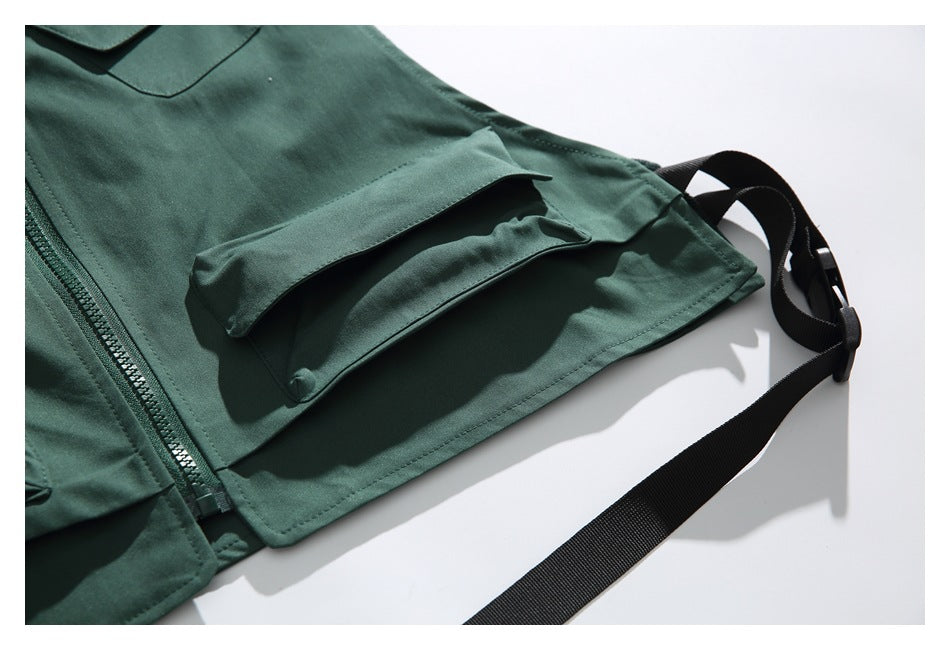Close-up of a dark green garment's lower flap pocket, zipper, and attached black strap.