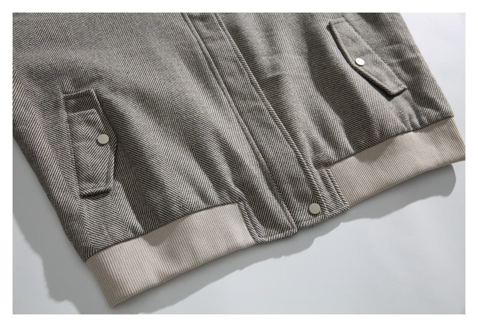 Close-up of the gray herringbone jacket's lower front, snap buttons, flap pockets, and beige ribbed hem.