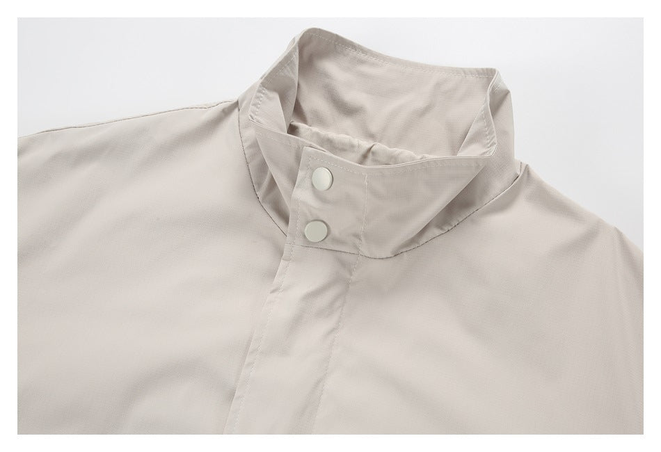 Close-up of a light beige jacket's stand collar with two pale snap buttons on the front placket.