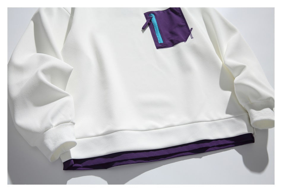 Close view of a white sweatshirt laid flat, showing a purple chest pocket with a turquoise zipper and purple hem trim.