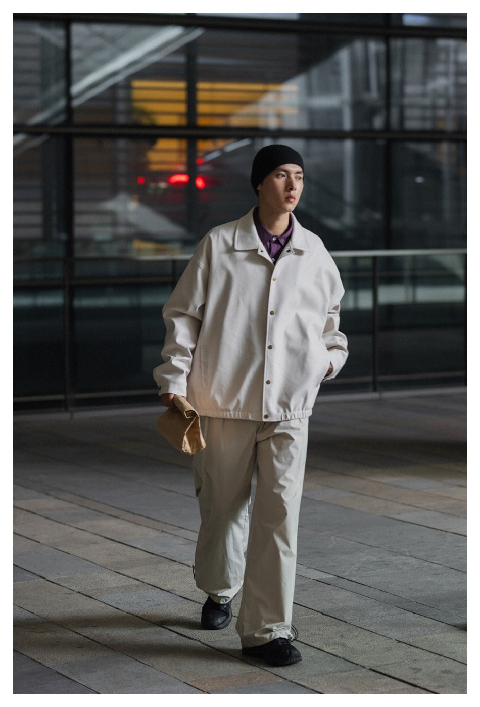 Full-length model wearing a light beige snap-front jacket, matching loose trousers, and a black beanie.