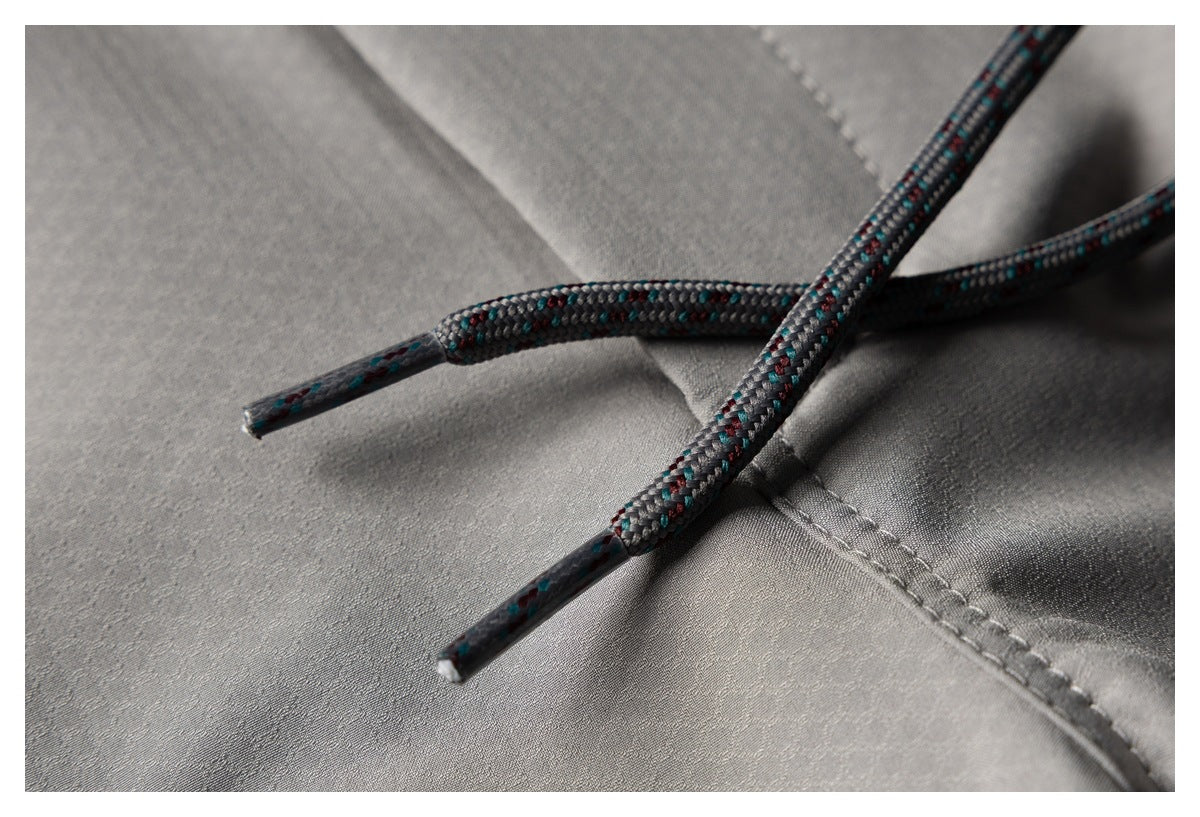 Close-up of two multicolored drawcord ends against gray trouser fabric and stitching.