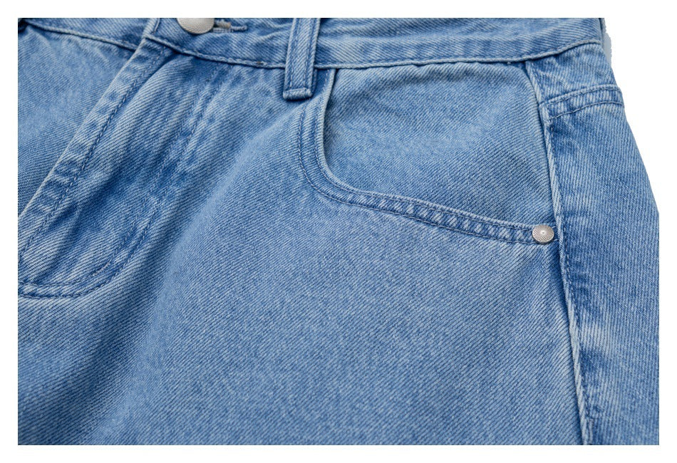 Close-up of light blue jeans showing a curved front pocket, waistband, belt loop and metal rivet.
