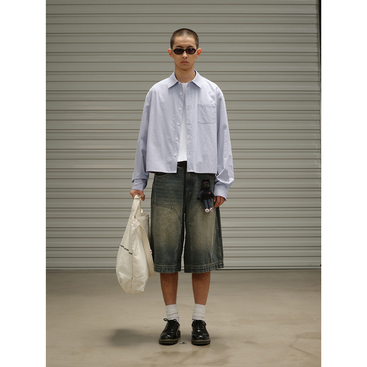 Full-length view of a model wearing a pale blue button-up shirt with a chest pocket, styled with denim shorts.