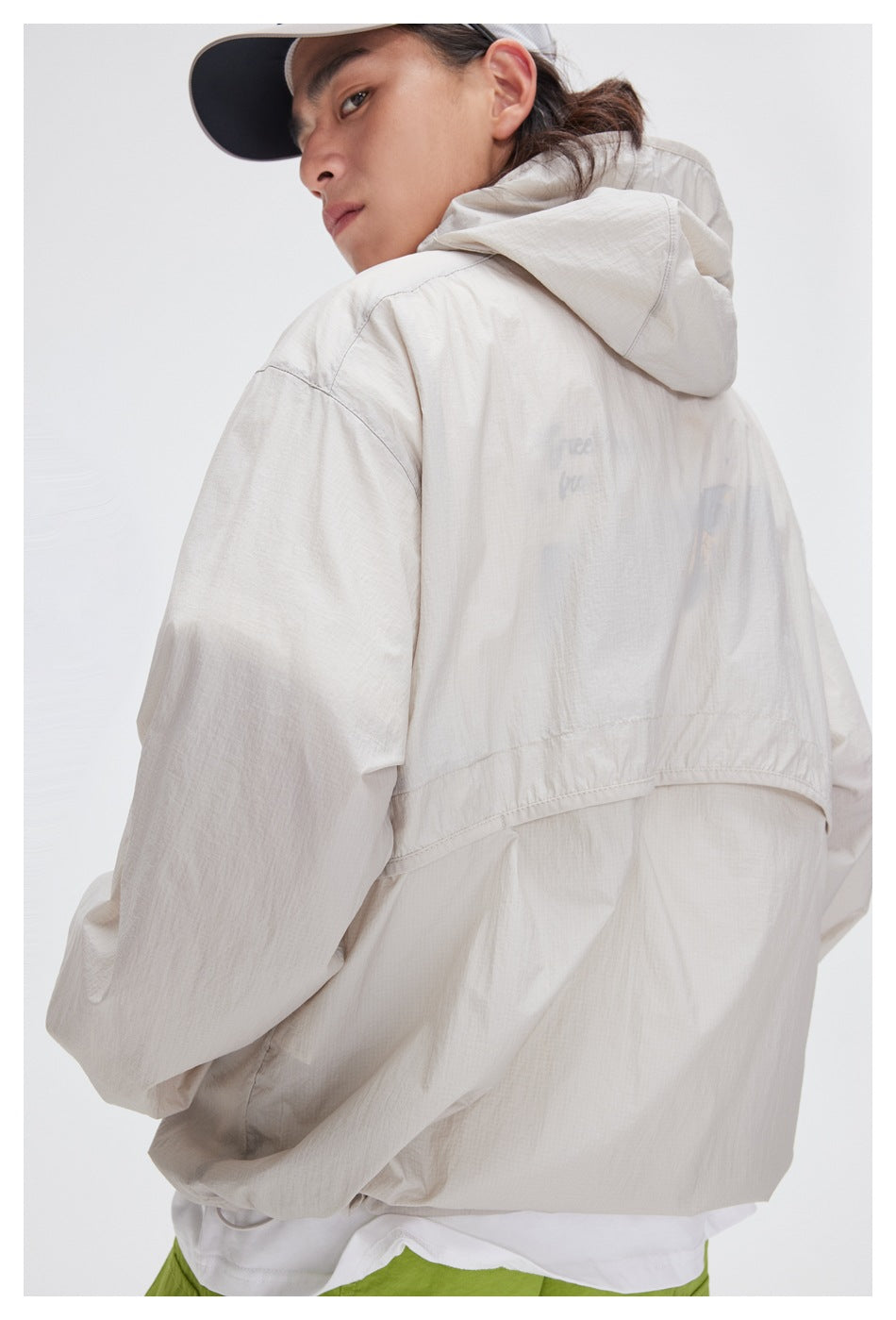 Close rear view of a model wearing a pale beige hooded jacket with a flap across the back.