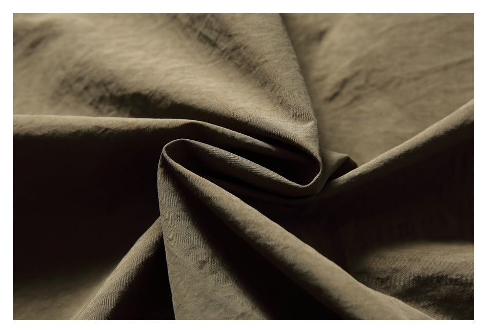 Close-up of olive-brown fabric arranged in soft folds, showing a fine textured surface.