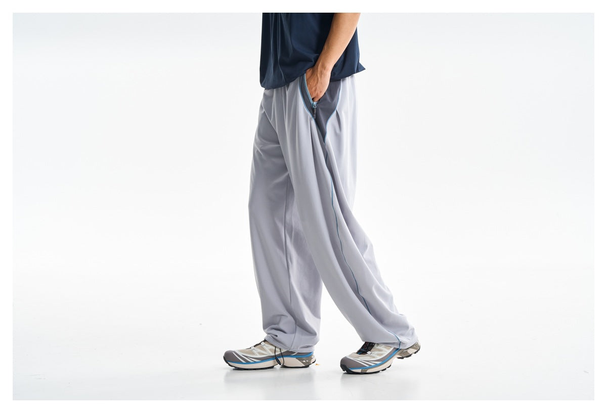 Side view of a model wearing loose light gray pants with blue piping and a zippered side pocket.