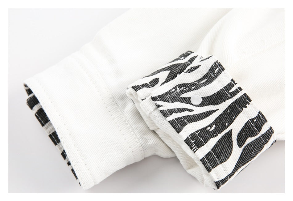 Close-up of a white denim cuff with a black zebra-print strap and a metal snap.