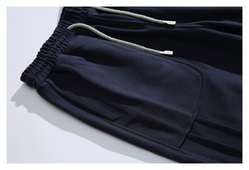 Close-up of dark navy pants showing an elastic waistband, light braided drawstrings and a curved pocket.