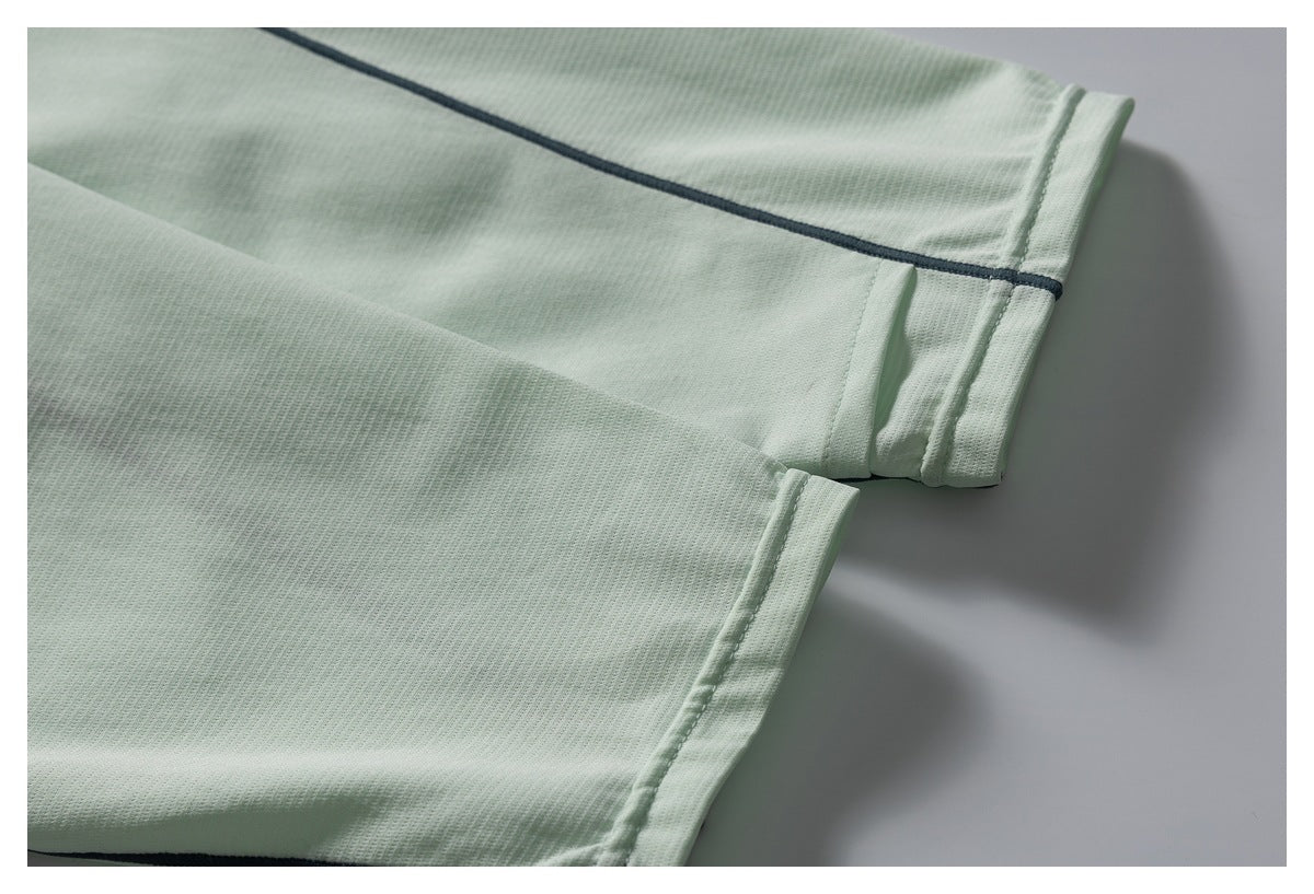 Close-up of pale mint-green garment hems with dark piping on one edge.