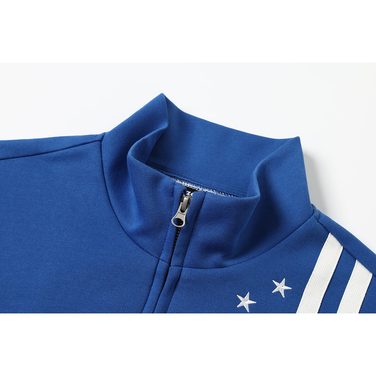Close-up of a blue track jacket’s stand collar, zipper, white star embroidery, and shoulder stripes.