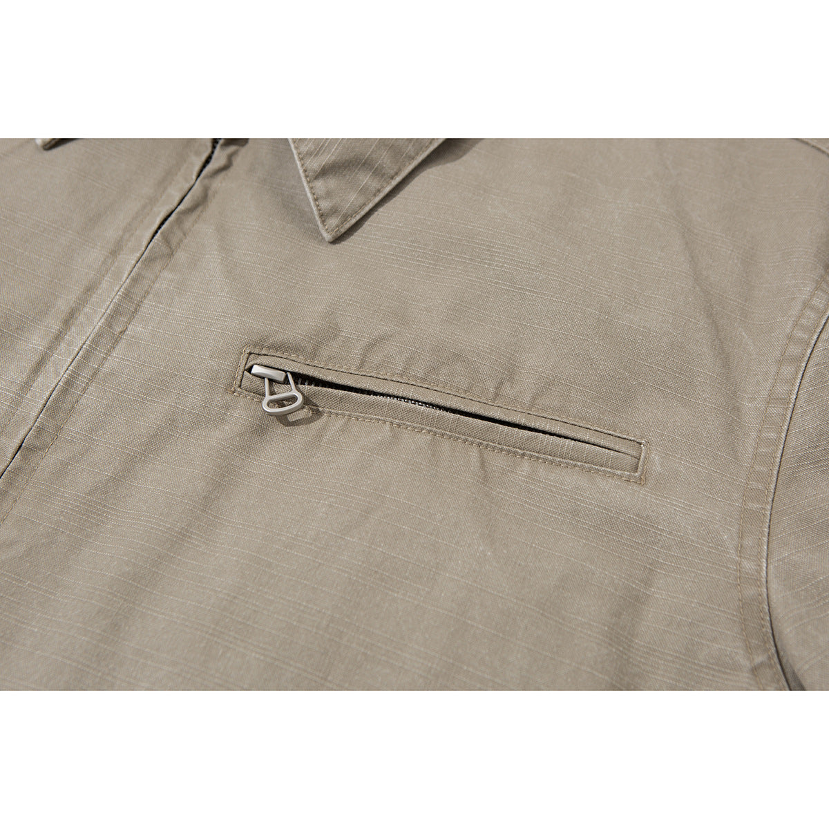 Close-up of a taupe jacket's horizontal zippered chest pocket and metal pull.