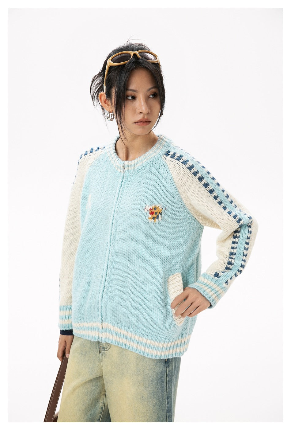 Three-quarter view of a model wearing a pale blue zip cardigan with cream patterned sleeves and striped ribbed edges.