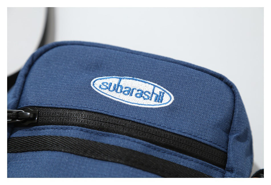 Close-up of a navy bag with a blue-and-white oval embroidered label and black zip trim.