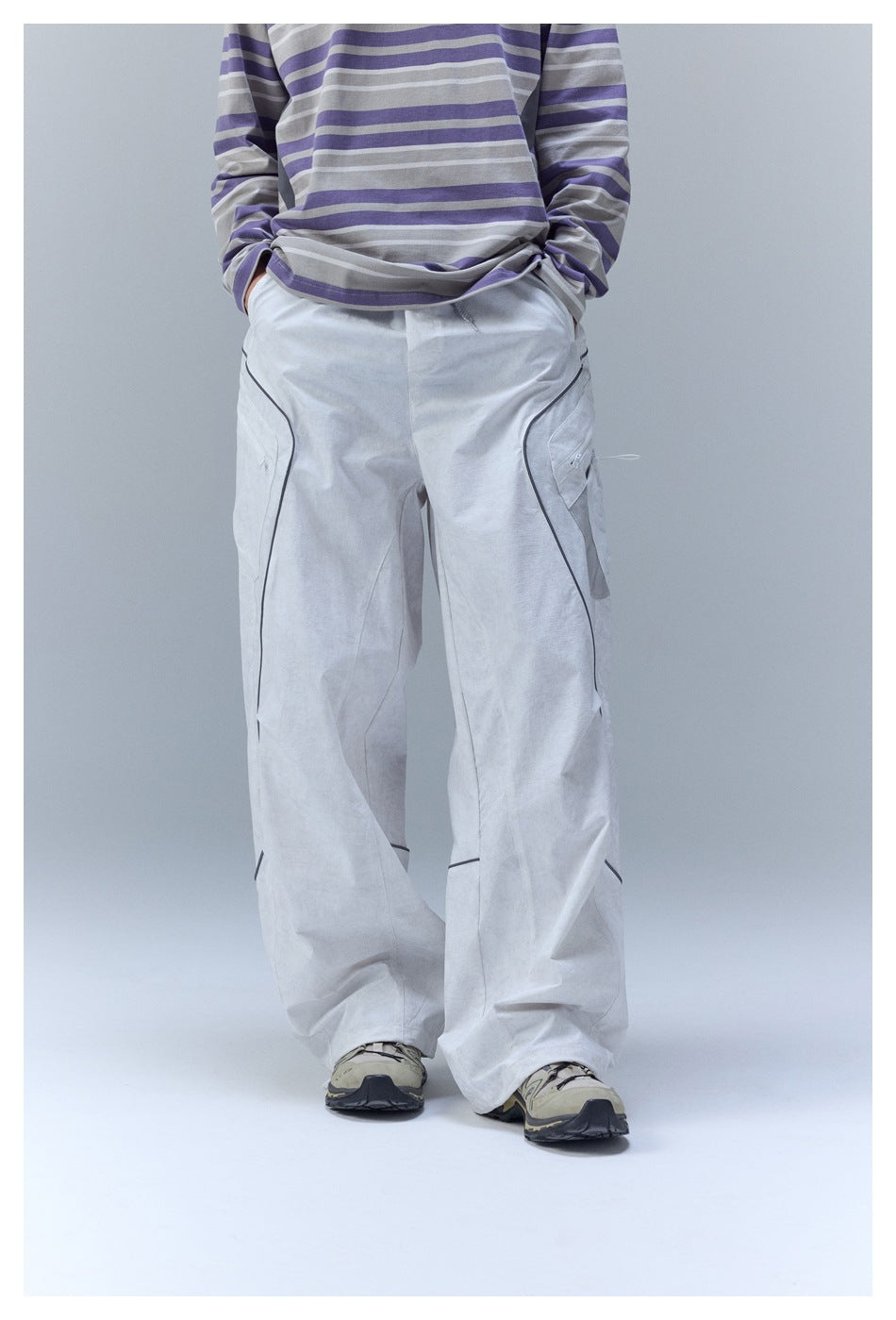 Model wearing loose light gray cargo pants with dark piping and a gray-and-purple striped shirt.