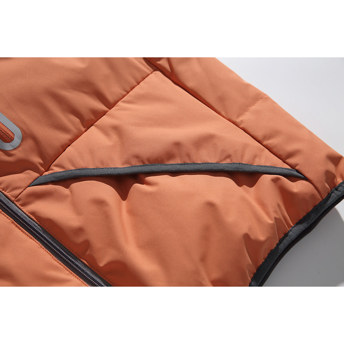 Close-up of the rust-orange vest's lower side pocket area, curved dark piping, and quilted seams.