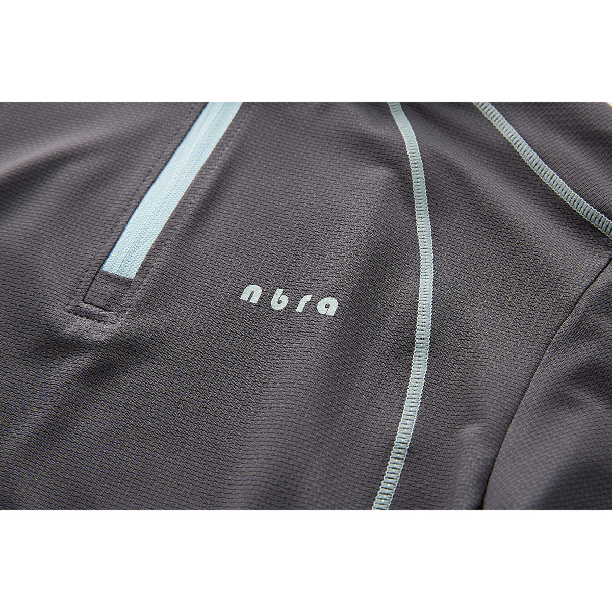 Close-up of a charcoal top with pale blue seam stitching, zipper detail and small chest lettering.
