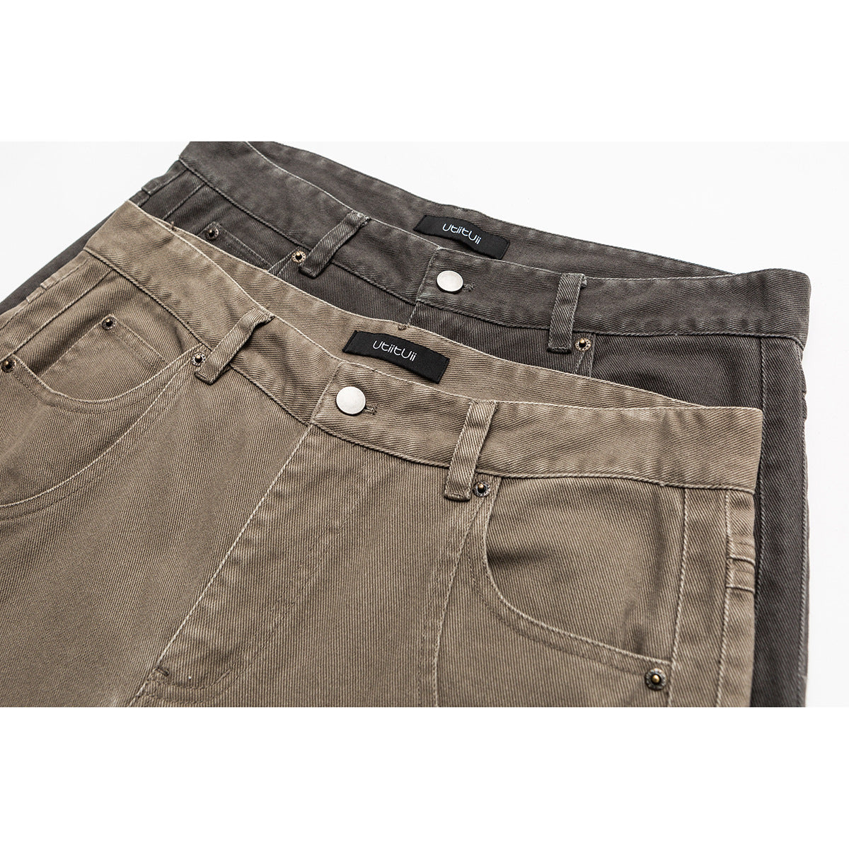 Close-up of two wide-leg trousers in taupe and charcoal, showing waistbands, buttons, belt loops and pockets.