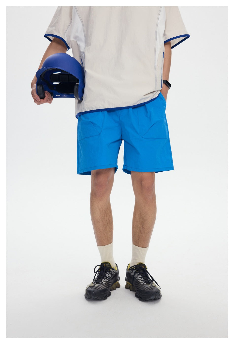 Model wearing bright blue shorts and an off-white short-sleeve top with blue trim, holding a blue helmet.