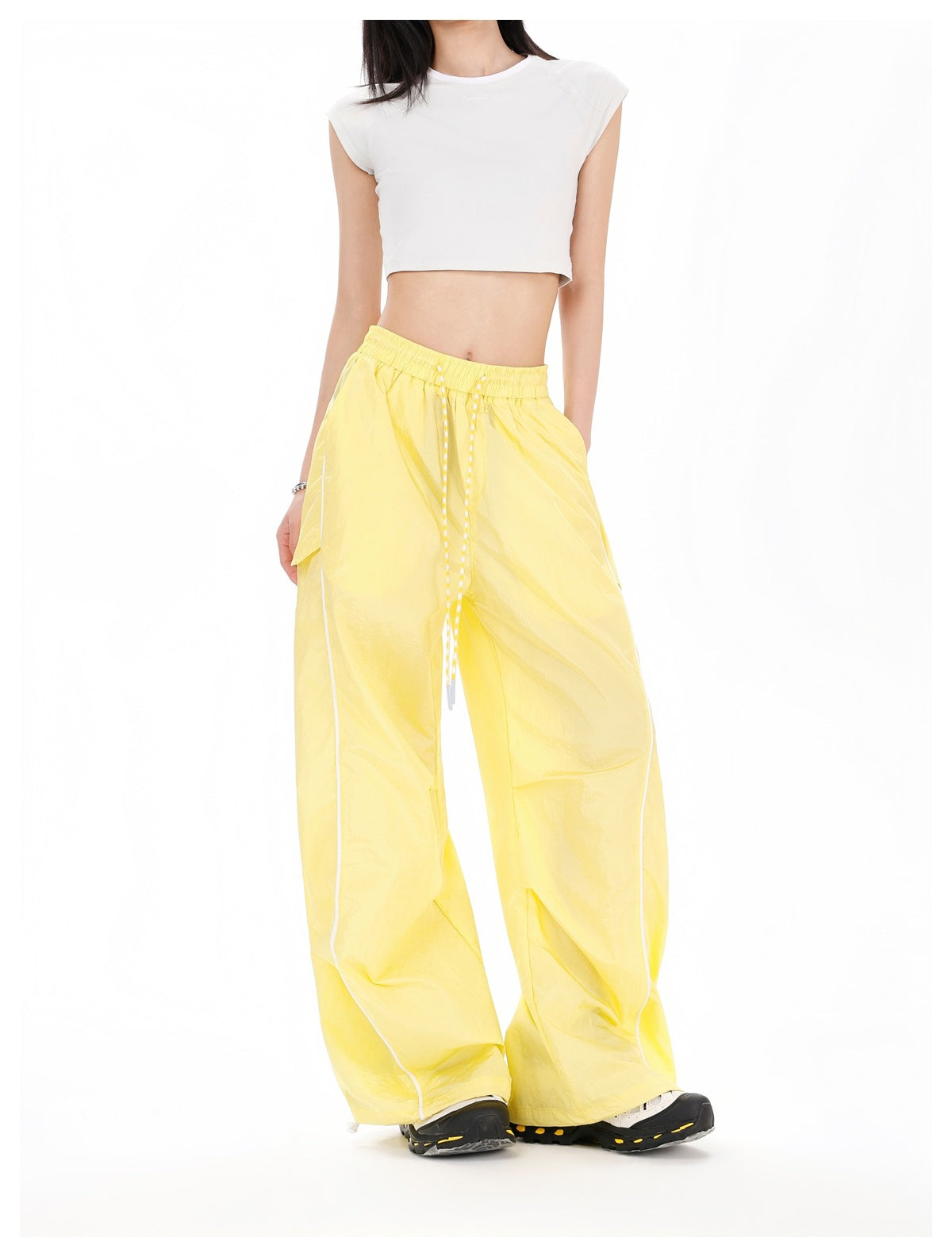 Front view of a model wearing bright yellow wide-leg pants with a drawstring waist, pockets, and white side piping.