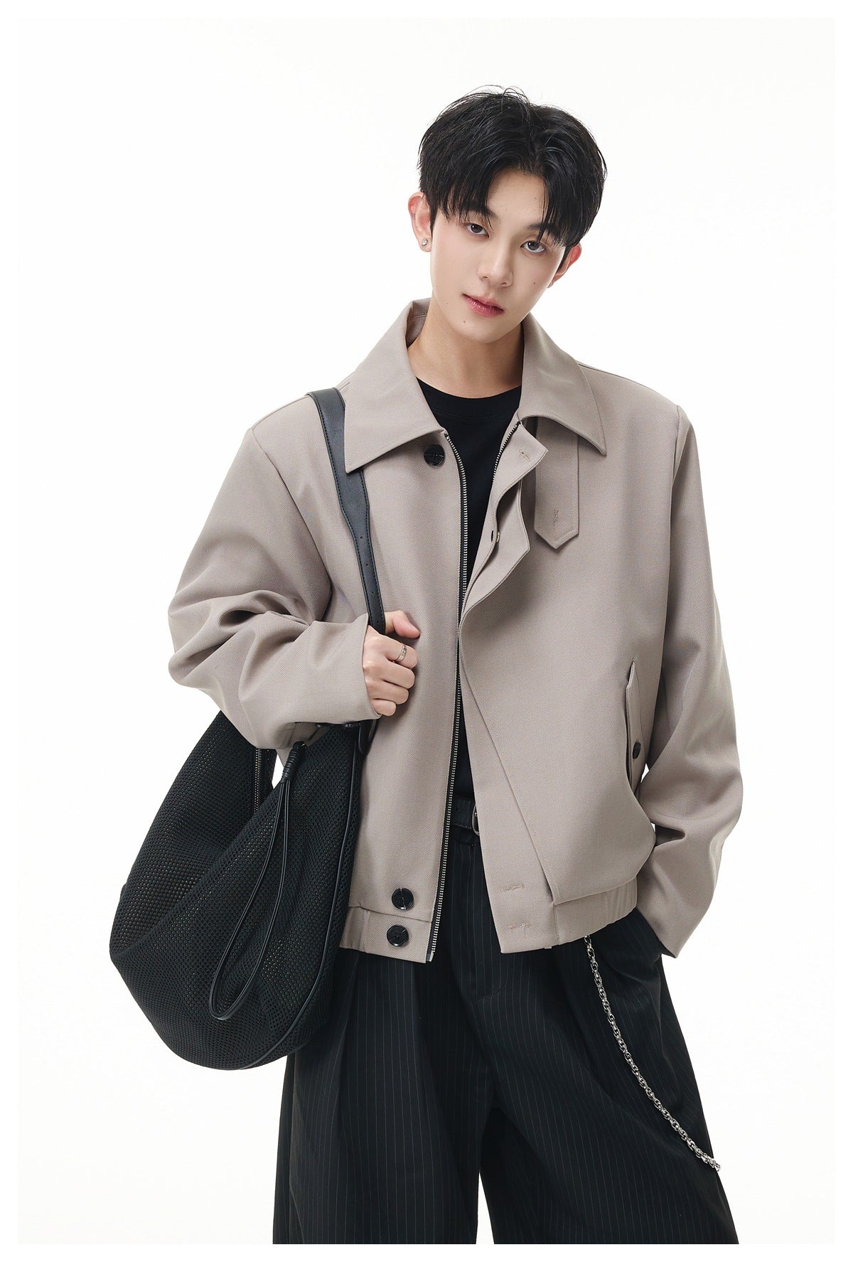 Model wearing an open taupe jacket with a broad collar, asymmetric front and angled buttoned pockets.