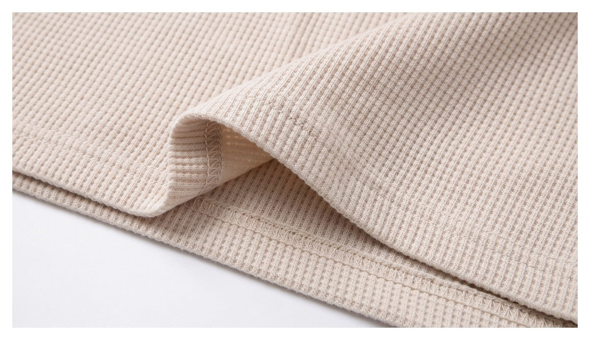 Close-up of cream waffle-knit fabric showing a folded hem and overlock stitching.