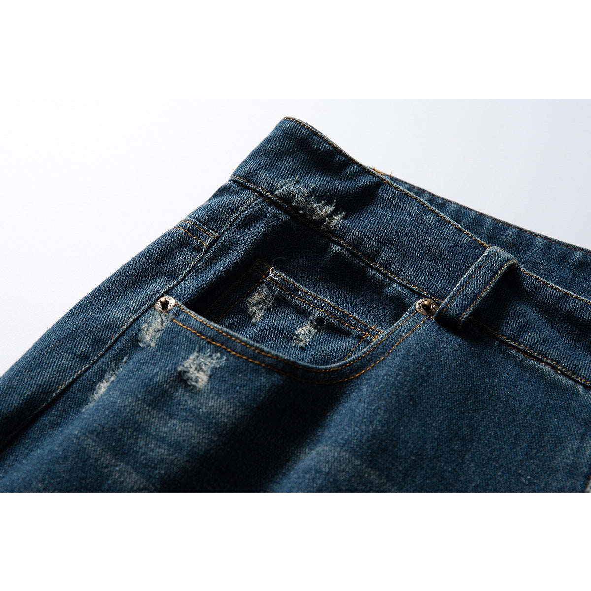 Close-up of dark blue distressed jeans showing the waistband, coin pocket, rivets and orange stitching.