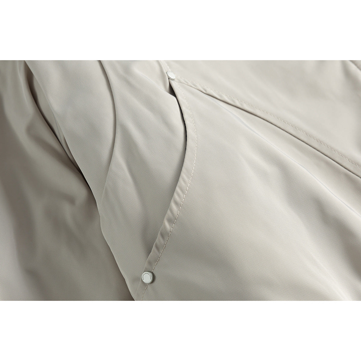 Close-up of light gray jacket fabric, a stitched seam, and snap buttons.