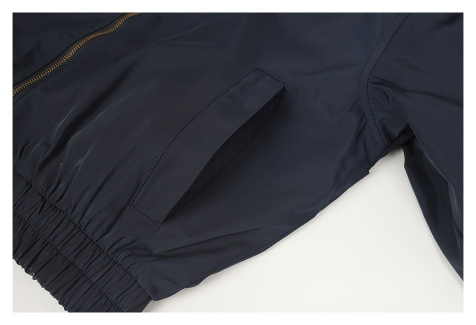 Close-up of a dark jacket's slanted pocket, gold zipper, and gathered elastic hem.