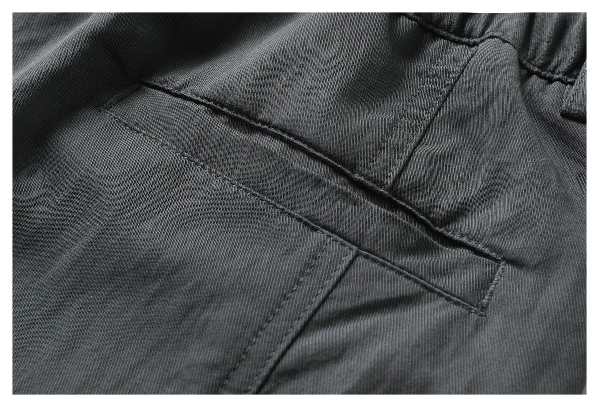 Close-up of dark charcoal garment fabric with intersecting stitched seams and a pocket edge.