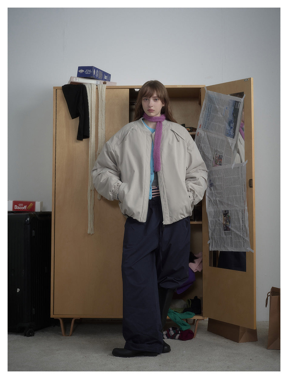 Model wearing a light beige-gray oversized zip jacket with navy trousers and a purple scarf, shown full length.