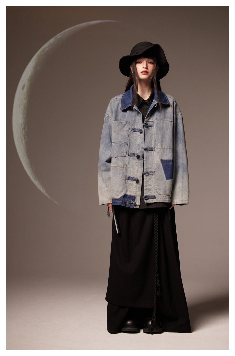 Model wearing washed blue denim jacket with knot closures over black shirt and long black skirt, front view
