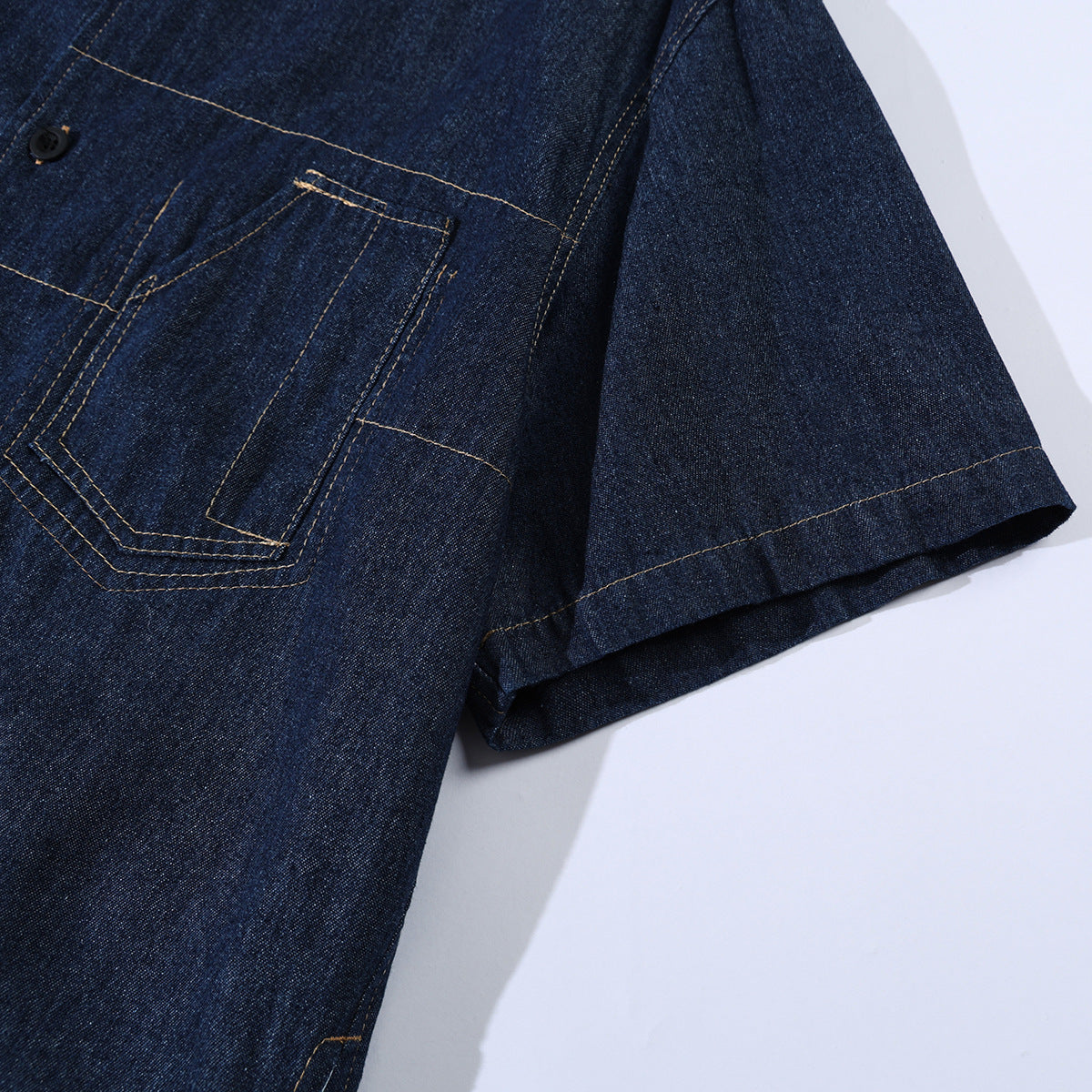Close-up of a dark indigo denim shirt showing its contrast-stitched chest pocket and short sleeve.