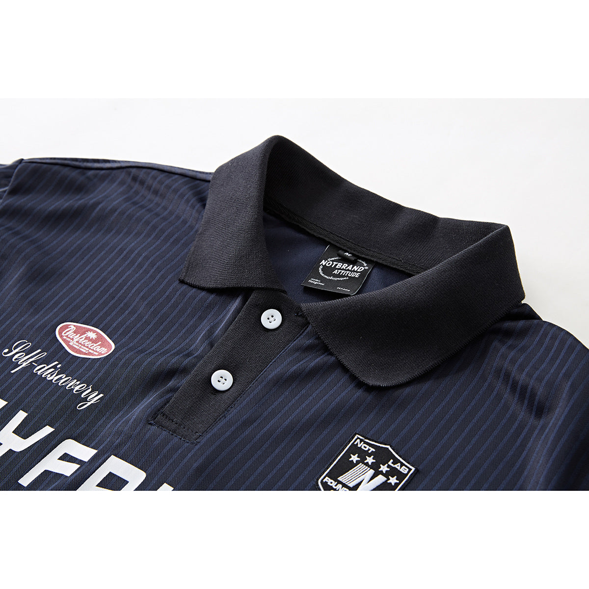 Close-up of a navy pinstriped polo shirt showing its black collar, white buttons, chest patches, and printed lettering.