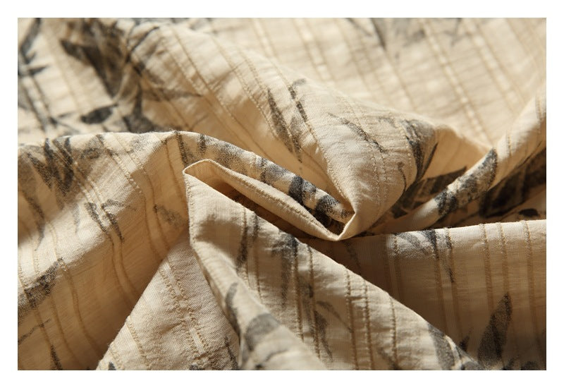 Close-up of beige fabric with an abstract brown and black pattern, shown in soft folds.