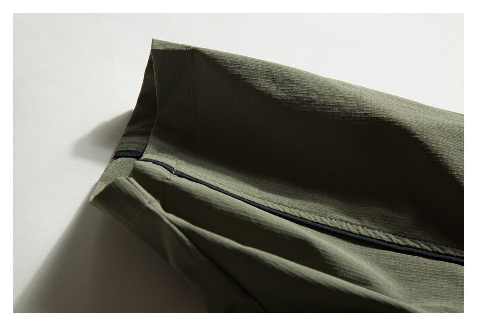Close-up of olive-green fabric with a folded edge and narrow dark piping along the seam.